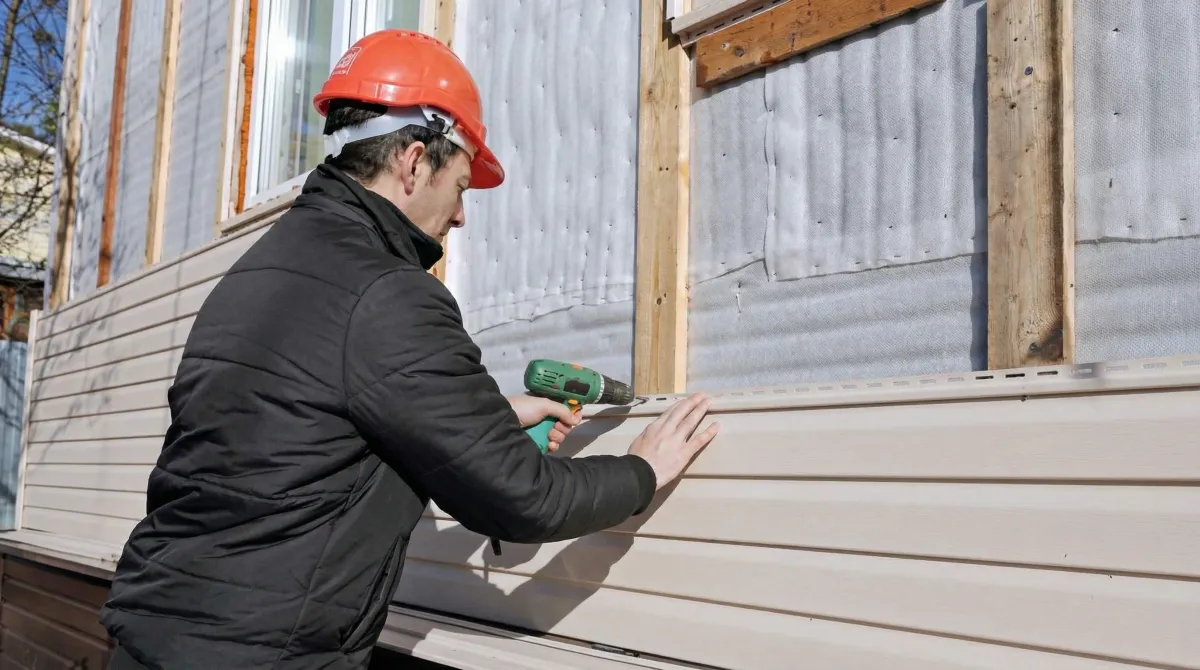 Siding replacement professional using a power drill to install new tan vinyl siding on a home exterior in Phoenix, AZ